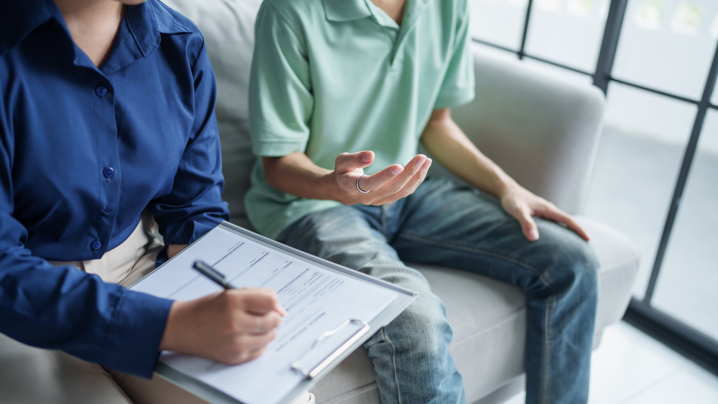 A care coordinator with a clipboard meets with a patient on a couch to walk through a recuperative-care plan